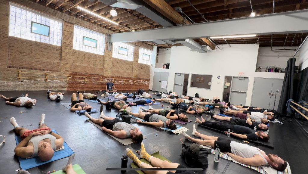 Group in savasana pose on mats in a brick-walled studio during a Paradigm Rhyme session