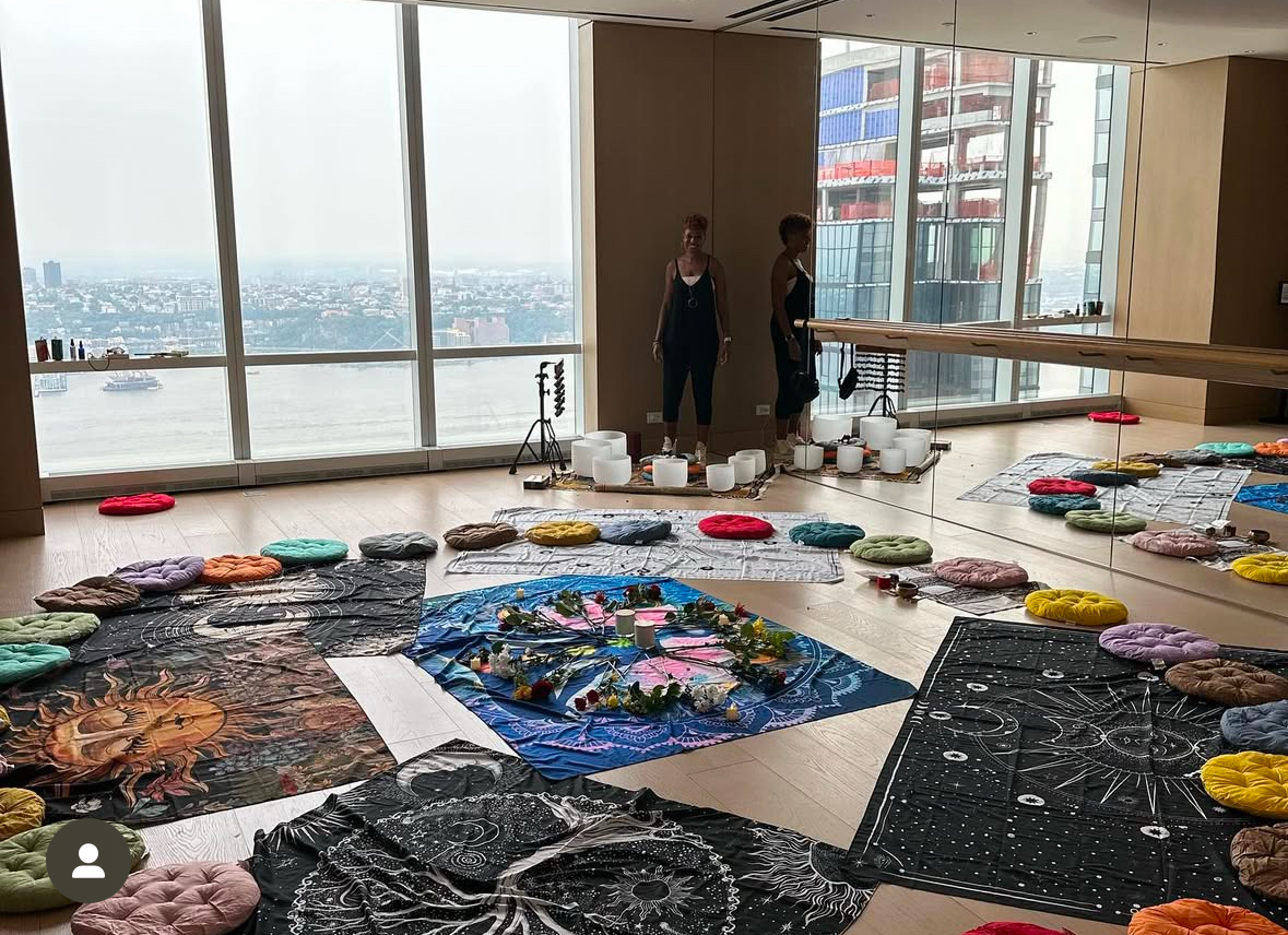 Sound bath setup with crystal bowls and cushions on a high-rise rooftop overlooking the city